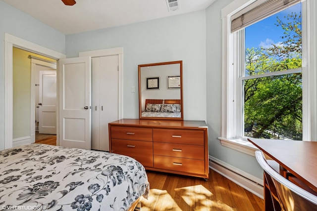 bedroom with baseboard heating, multiple windows, wood finished floors, and baseboards