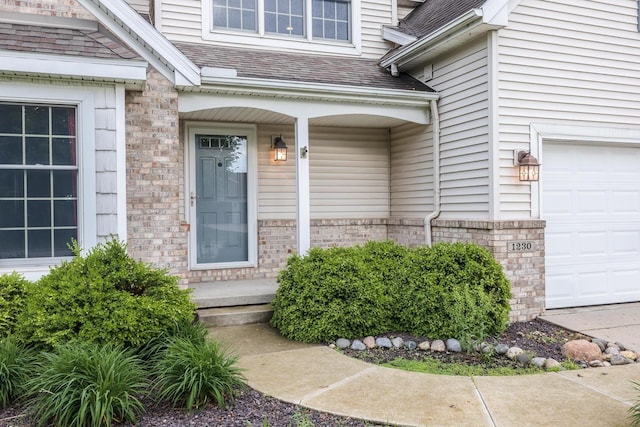 property entrance featuring a porch, a shingled roof, a garage, and brick siding