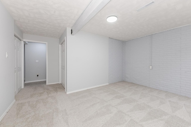 carpeted spare room featuring a textured ceiling, beam ceiling, baseboards, and brick wall