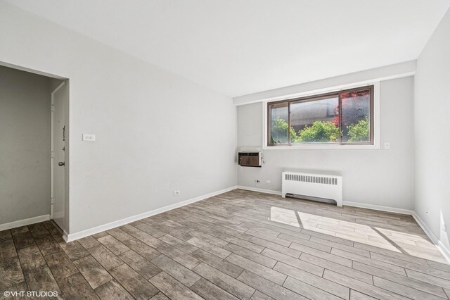 spare room with radiator, wood finished floors, baseboards, and an AC wall unit