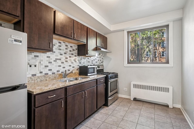 kitchen featuring radiator, appliances with stainless steel finishes, under cabinet range hood, a sink, and decorative backsplash