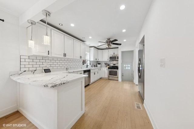 kitchen with stainless steel appliances, decorative backsplash, a peninsula, light wood-type flooring, and white cabinetry