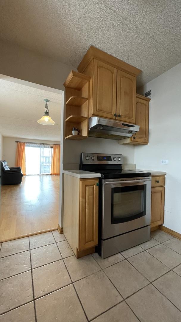 6221 N Niagara Ave Unit 401, Chicago, IL 60631 - kitchen with electric stove, under cabinet range hood, light tile patterned flooring, a textured ceiling, and light countertops