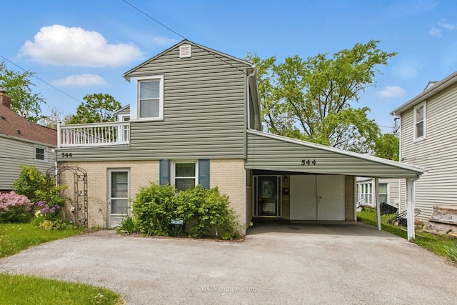 view of front of house with driveway, brick siding, a balcony, and an attached carport