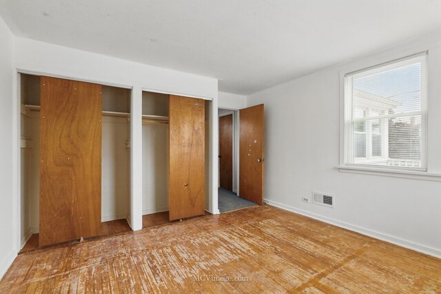 unfurnished bedroom with two closets, wood finished floors, and baseboards