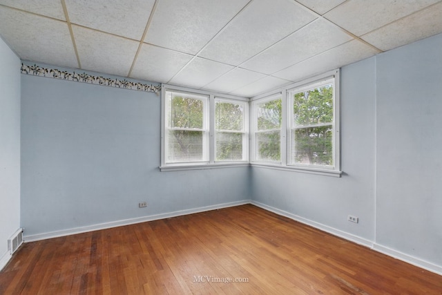 empty room featuring a drop ceiling, hardwood / wood-style floors, and baseboards