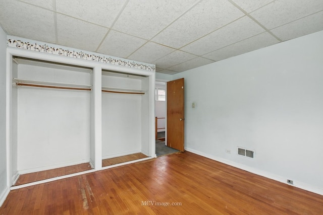 unfurnished bedroom with a drop ceiling, baseboards, and wood finished floors