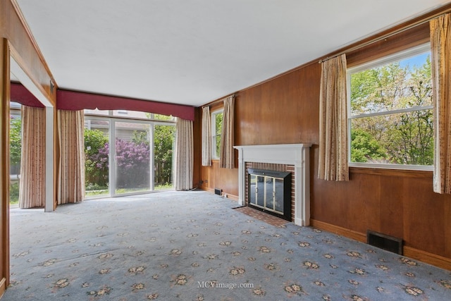unfurnished living room with carpet, a fireplace, wooden walls, healthy amount of natural light, and baseboards