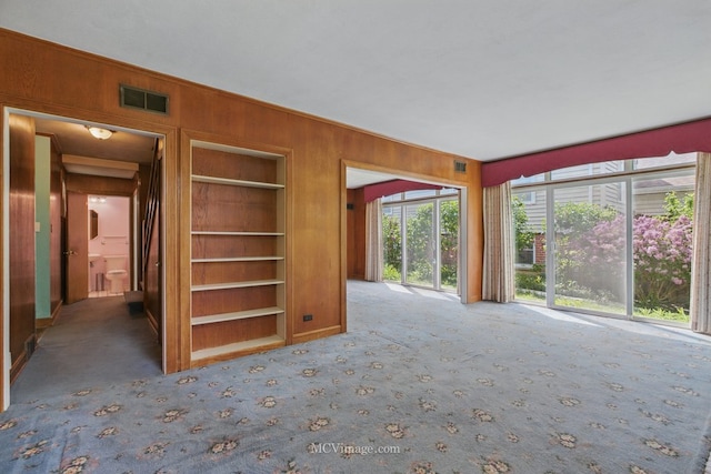 unfurnished living room featuring wood walls, built in features, and carpet