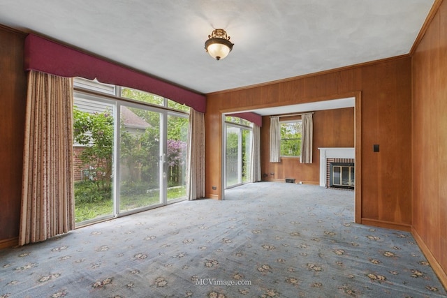 unfurnished living room with carpet floors, wood walls, a brick fireplace, and baseboards