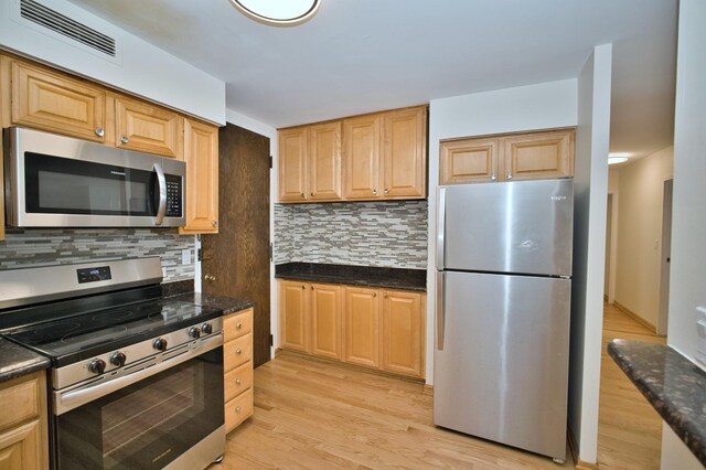 6007 N Sheridan Rd Unit 25F, Chicago, IL 60660 - kitchen featuring appliances with stainless steel finishes, decorative backsplash, light wood-style flooring, light brown cabinetry, and dark stone countertops