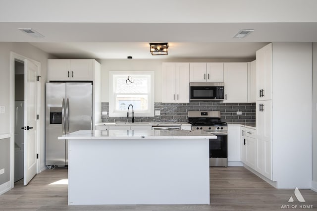 kitchen featuring stainless steel appliances, a sink, backsplash, and light wood-style flooring