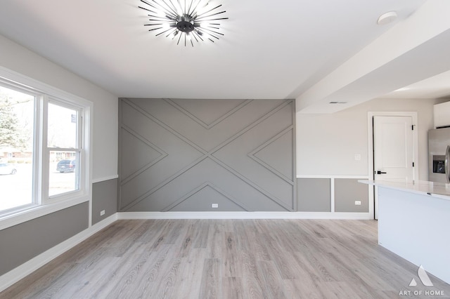 empty room with light wood-type flooring, baseboards, a chandelier, and a decorative wall