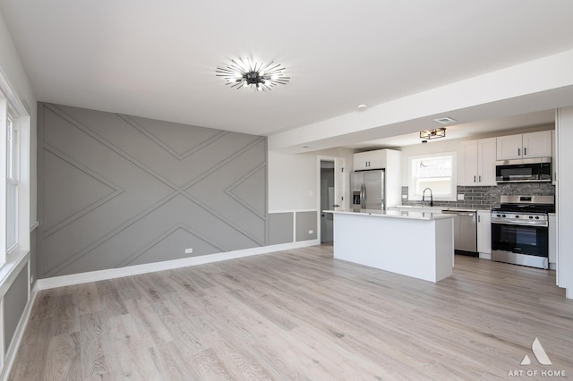 kitchen with appliances with stainless steel finishes, a sink, light wood finished floors, a kitchen island, and light countertops