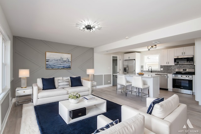 living room with light wood-style flooring, a decorative wall, and baseboards