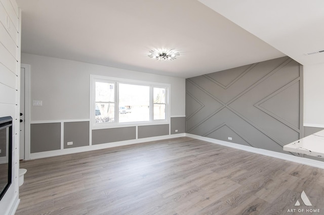 unfurnished living room featuring light wood-type flooring, a decorative wall, and baseboards