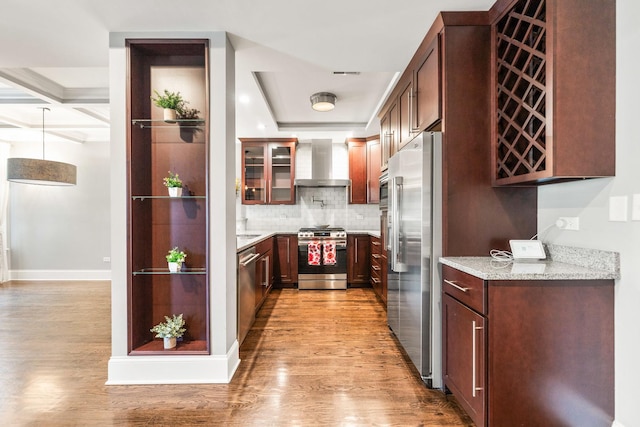 kitchen with stainless steel appliances, wall chimney exhaust hood, light wood-style floors, decorative backsplash, and light stone countertops