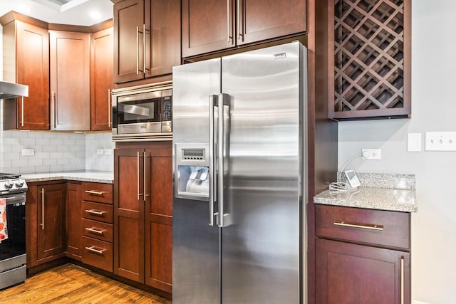 kitchen featuring appliances with stainless steel finishes, light wood-style floors, wall chimney exhaust hood, light stone countertops, and backsplash