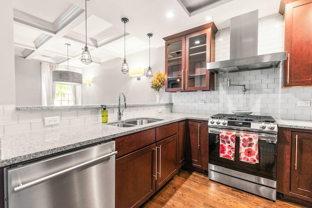 kitchen featuring appliances with stainless steel finishes, wall chimney range hood, a sink, glass insert cabinets, and decorative light fixtures
