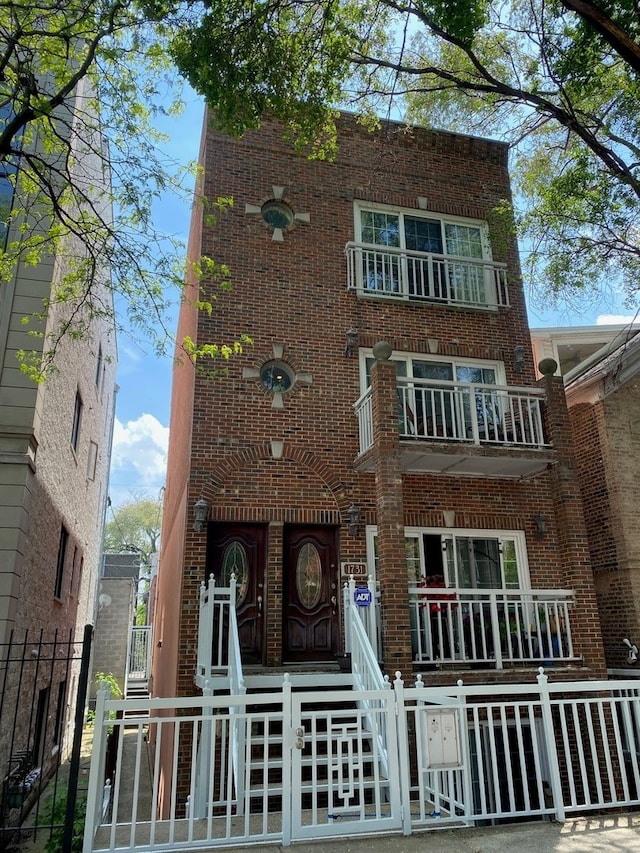 view of front of house featuring brick siding, a balcony, a fenced front yard, and a gate