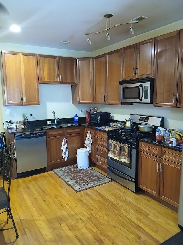 kitchen with appliances with stainless steel finishes, a sink, dark countertops, light wood-type flooring, and recessed lighting