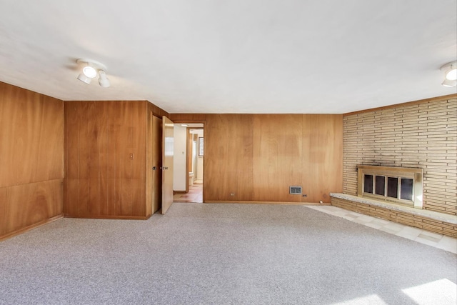 unfurnished living room featuring wooden walls, a brick fireplace, and carpet floors