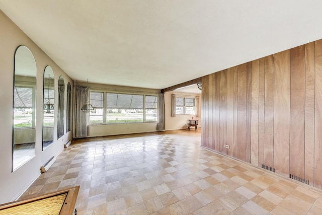 unfurnished room with wood walls, a baseboard radiator, arched walkways, and light floors
