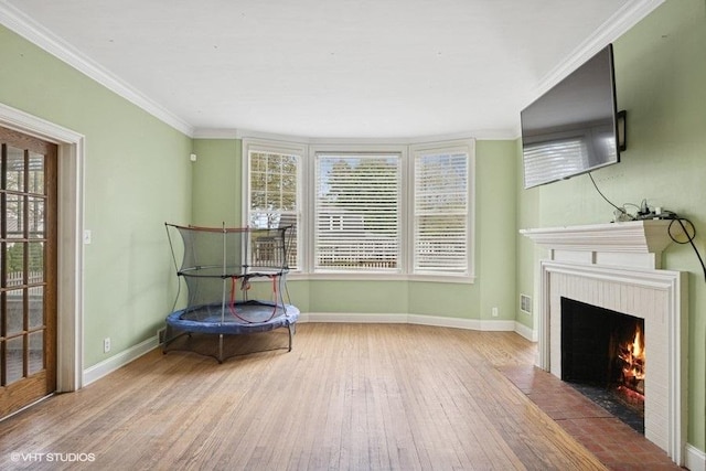 sitting room with wood finished floors, a fireplace with flush hearth, baseboards, and crown molding