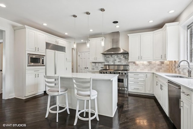 kitchen featuring wall chimney range hood, built in appliances, a sink, a center island, and light countertops