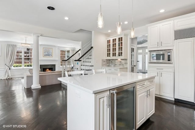 kitchen featuring beverage cooler, built in appliances, a warm lit fireplace, dark wood finished floors, and recessed lighting