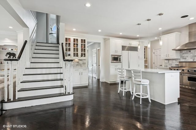 kitchen with wall chimney range hood, built in appliances, tasteful backsplash, white cabinets, and recessed lighting