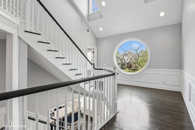 entrance foyer featuring a skylight, high vaulted ceiling, a wainscoted wall, wood finished floors, and a decorative wall