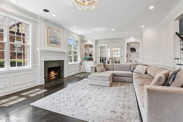 living area featuring crown molding, a warm lit fireplace, healthy amount of natural light, wood finished floors, and built in shelves