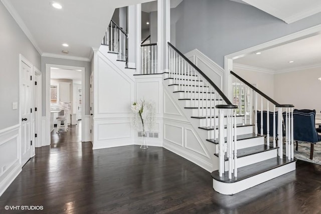 stairs featuring a decorative wall, wood finished floors, crown molding, recessed lighting, and a wainscoted wall
