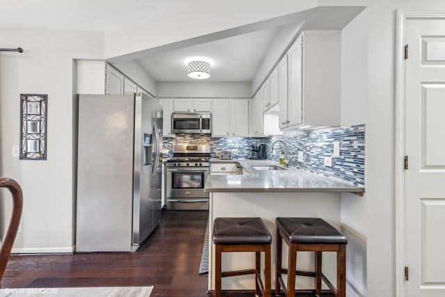 kitchen with stainless steel appliances, a sink, a peninsula, tasteful backsplash, and dark wood finished floors