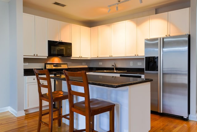 kitchen with stainless steel appliances, a sink, light wood finished floors, and a breakfast bar