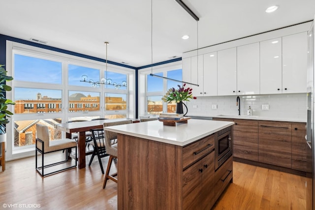 1203 E 46th St Unit 4N, Chicago, IL 60653 - kitchen featuring a sink, stainless steel microwave, white cabinets, light wood finished floors, and modern cabinets