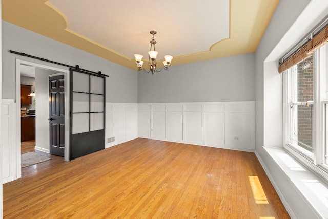 24006 Skyler Ln, Plainfield, IL 60586 - unfurnished room with light wood-style floors, a barn door, a chandelier, a wainscoted wall, and a decorative wall