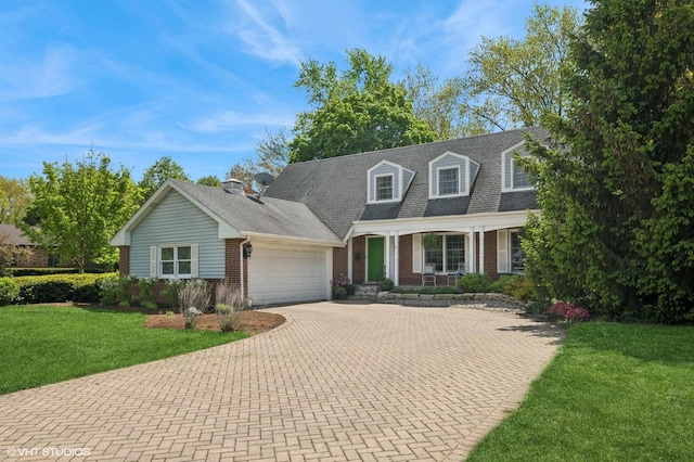 new england style home with brick siding, an attached garage, decorative driveway, a front yard, and covered porch