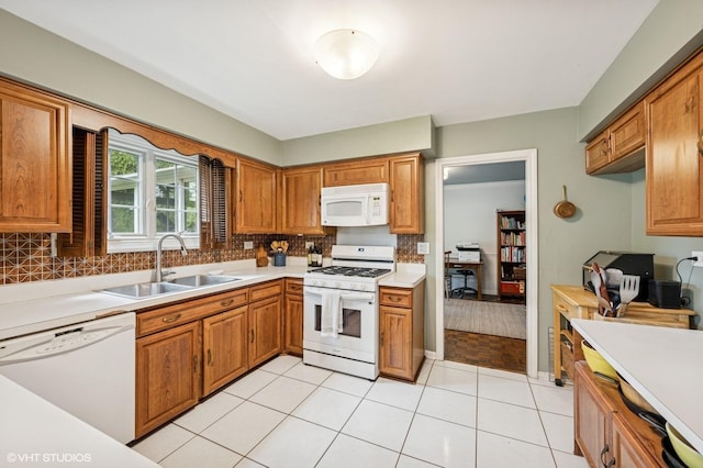 kitchen featuring white appliances, a sink, backsplash, light countertops, and brown cabinetry