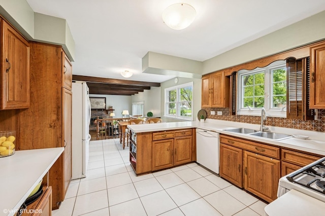 kitchen featuring white appliances, a sink, decorative backsplash, a peninsula, and brown cabinets
