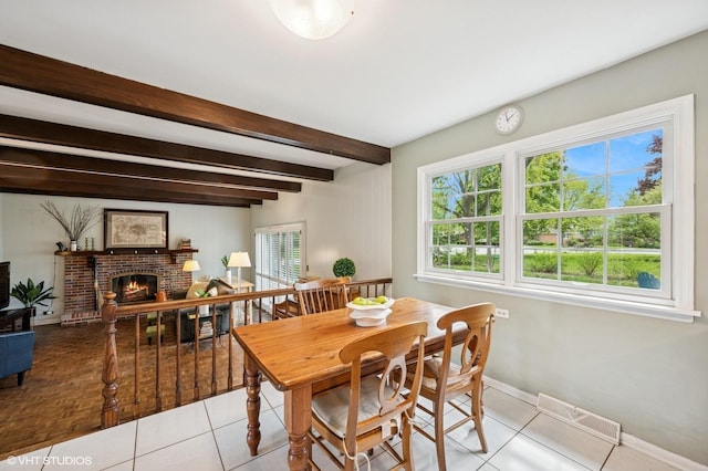 dining area featuring baseboards, beamed ceiling, a brick fireplace, and tile patterned floors
