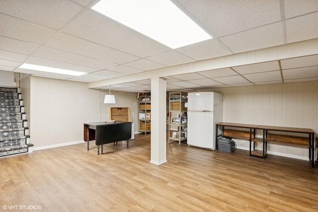 finished basement with freestanding refrigerator, a paneled ceiling, light wood-style flooring, and baseboards