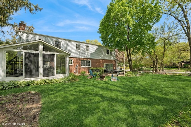 back of property featuring a sunroom, brick siding, a lawn, and a chimney