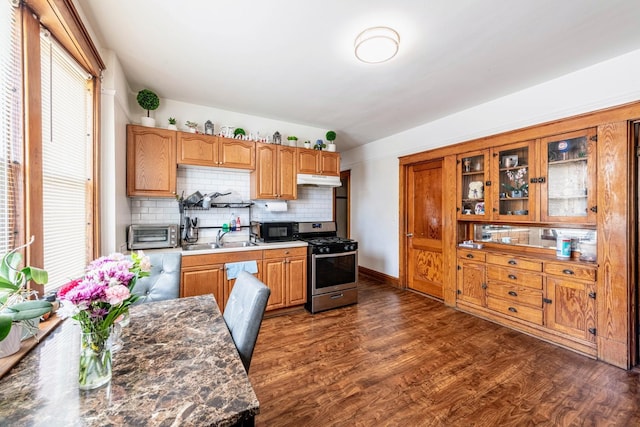 kitchen featuring gas stove, black microwave, backsplash, dark wood-style flooring, and glass insert cabinets
