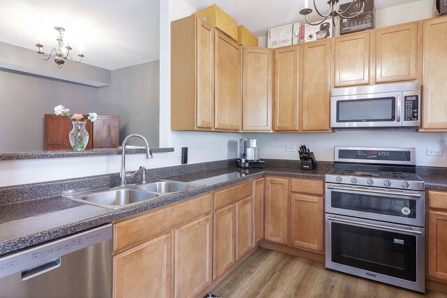 kitchen featuring stainless steel appliances, a sink, light wood finished floors, dark countertops, and light brown cabinetry