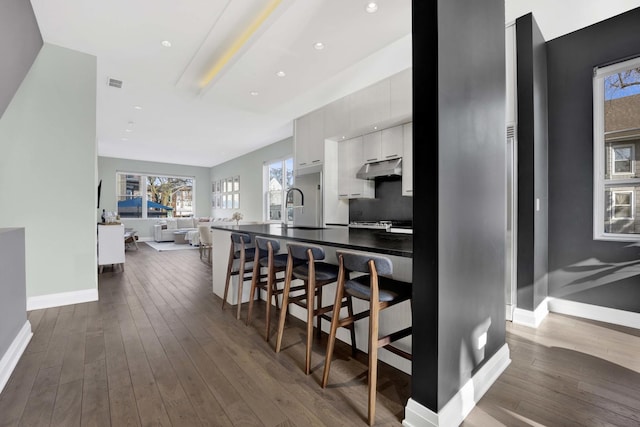 3056 N Monticello Ave, Chicago, IL 60618 - kitchen featuring a breakfast bar, dark wood-style floors, under cabinet range hood, baseboards, and white cabinetry