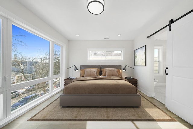 bedroom featuring a barn door, multiple windows, baseboards, recessed lighting, and ensuite bathroom