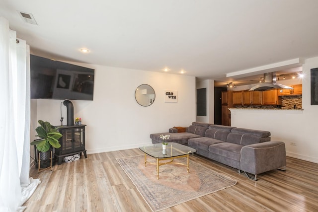 living area featuring a wood stove, light wood-type flooring, recessed lighting, and baseboards