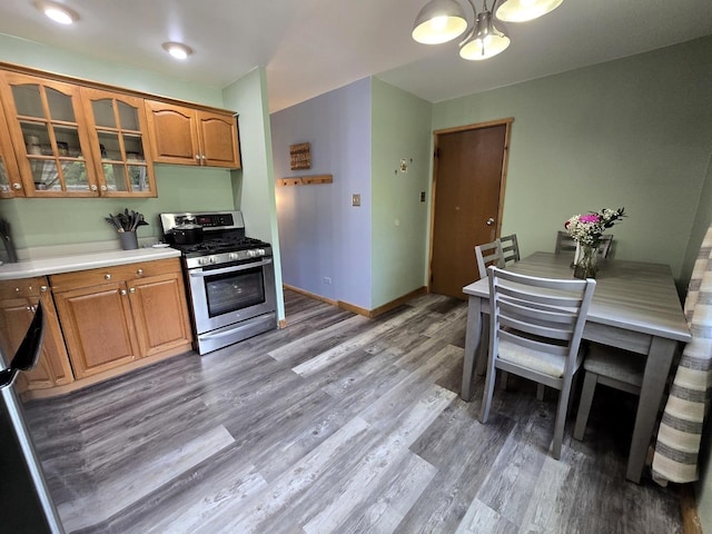 kitchen featuring stainless steel gas range, a chandelier, glass insert cabinets, brown cabinetry, and light wood finished floors